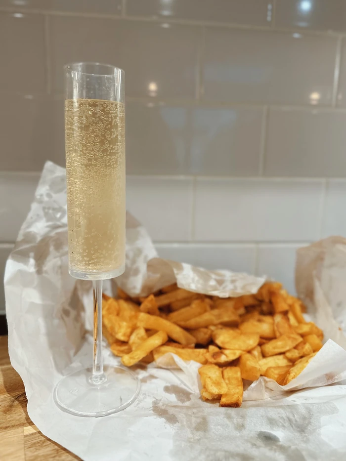 Champagne flute beside chips and paper wrapping on wooden table