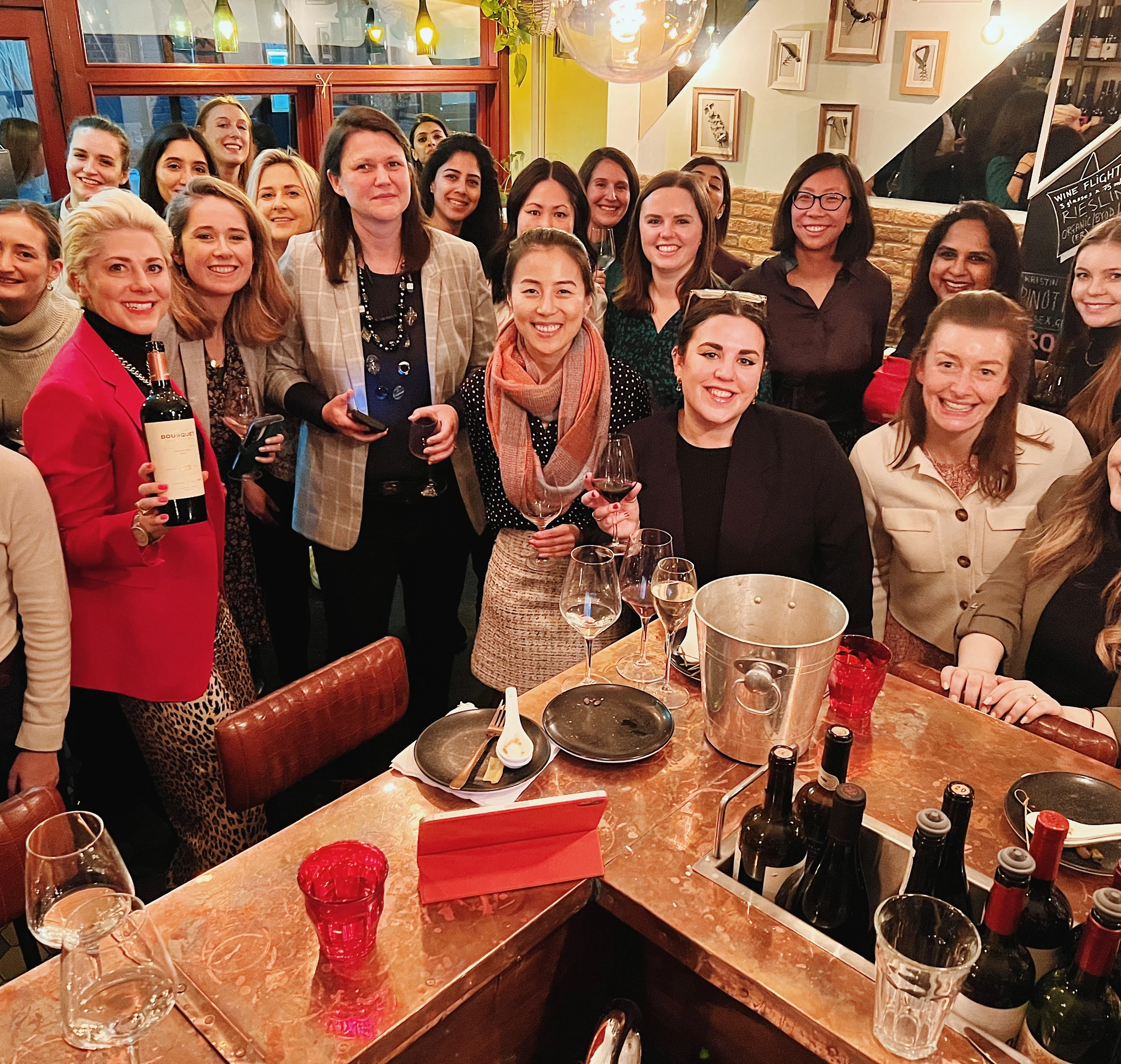 Group of women holding wine glasses and a bottle around a restaurant table