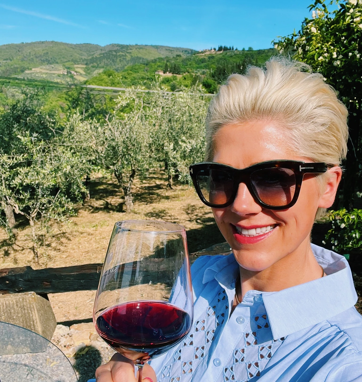 Elizabeth holds a glass of red wine beside Savignola's hillside vineyard in Tuscany