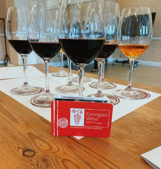 Six wine glasses filled with red, rosé and amber wine beside a Georgian Wine card