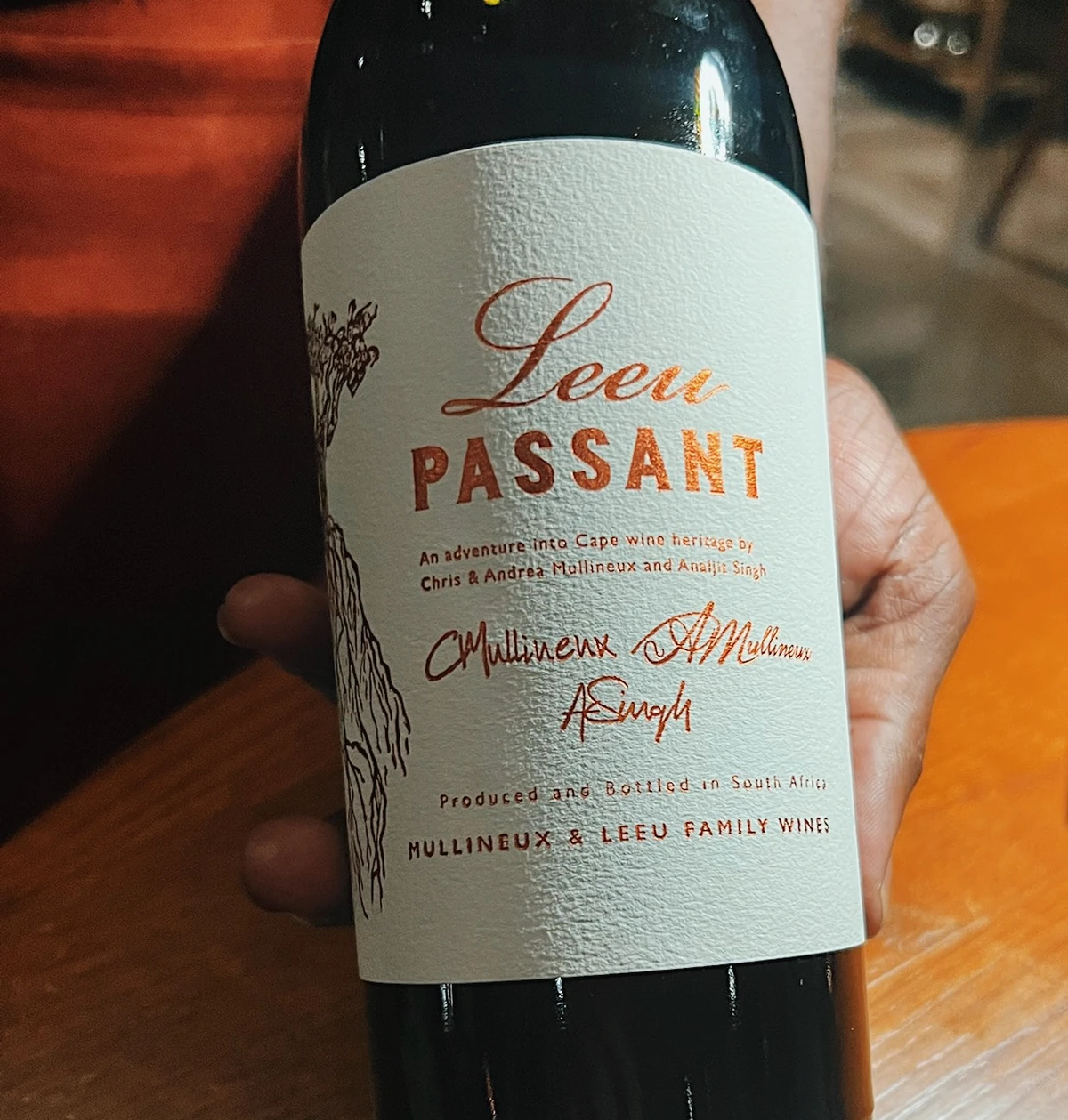 Close-up of a Leeu Passant wine bottle held over a wooden table
