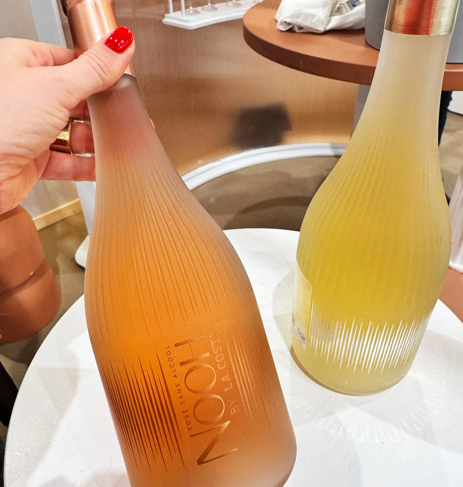 Two ribbed bottles of non-alcoholic drink, one pink and one pale yellow, displayed at a wine event