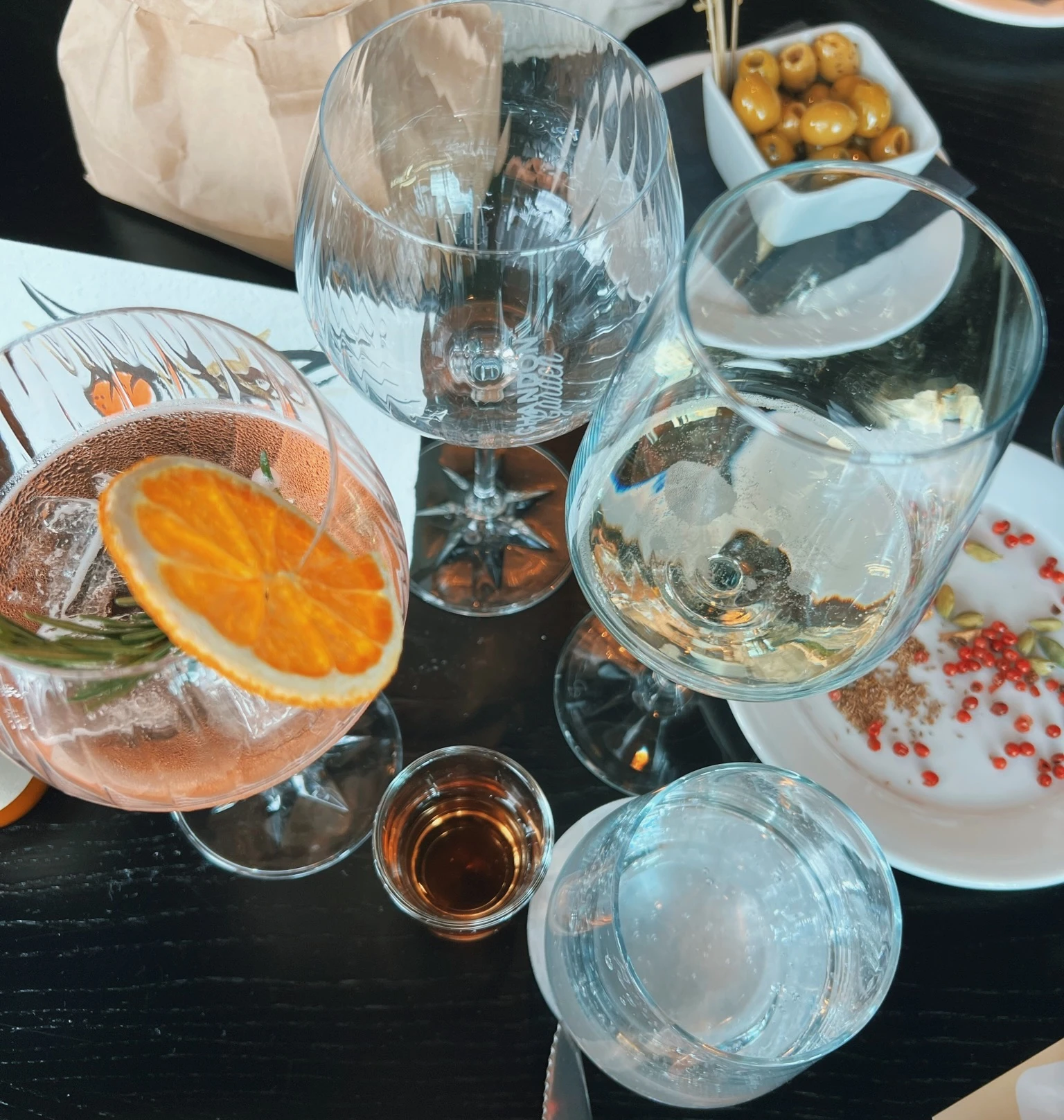 Wine glasses and cocktails with orange garnish, olives and snacks on a dark table