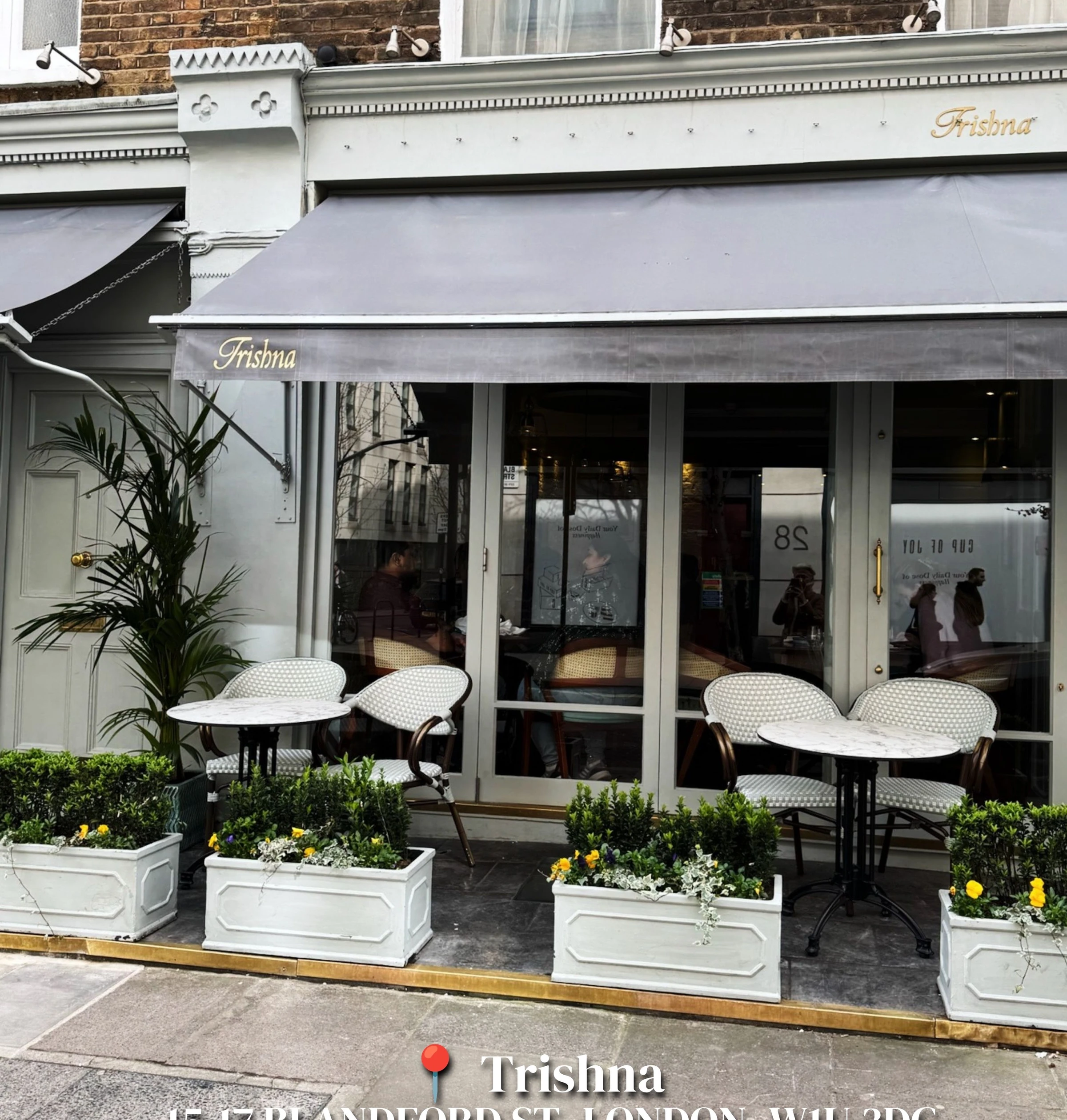 Trishna restaurant frontage with outdoor tables, chairs and flower planters in Marylebone, London