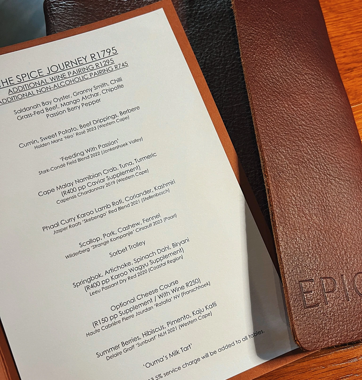 Printed tasting menu beside leather-bound menus on a wooden table
