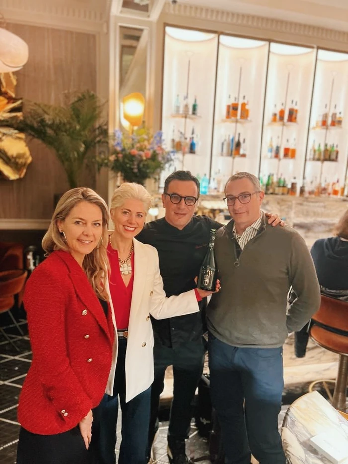 Four adults posing in a wine bar holding a bottle