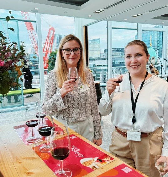 Two guests raise glasses of red wine at a corporate tasting in a bright city venue