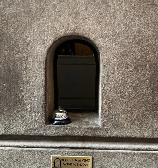Stone wine window with a service bell and plaque reading Buchetta del Vino Wine Window