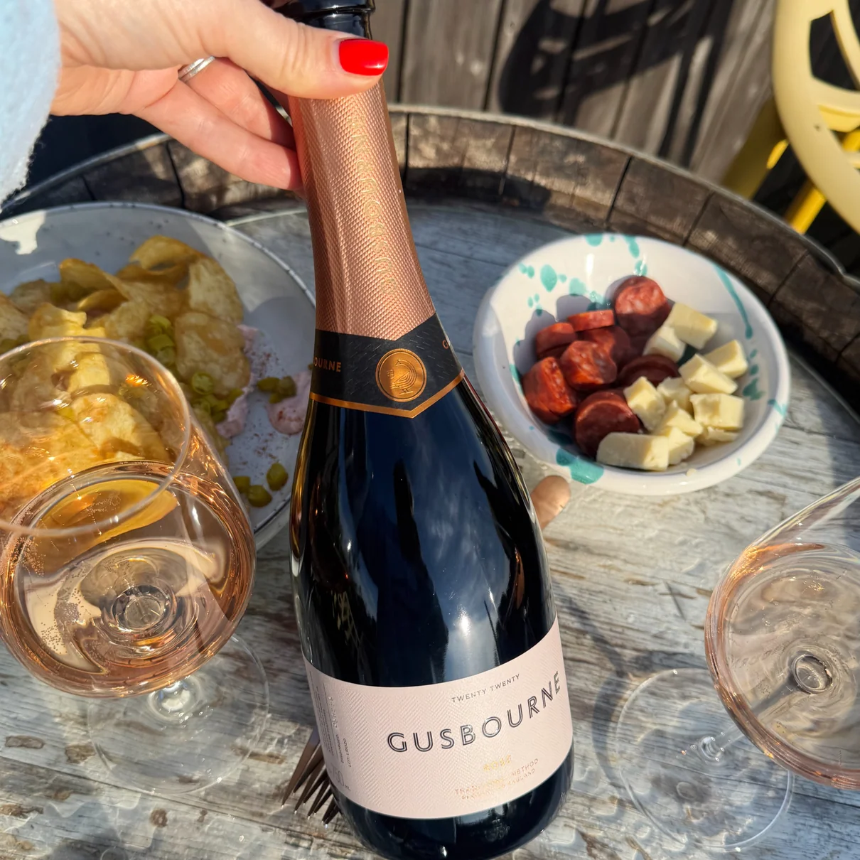 Rosé sparkling wine bottle with crisps, sausage and cheese bowls