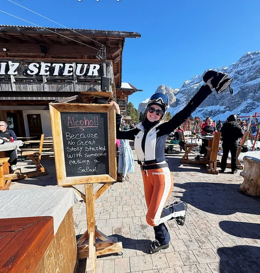 Skier raising a helmet beside a mountain restaurant in the Dolomites