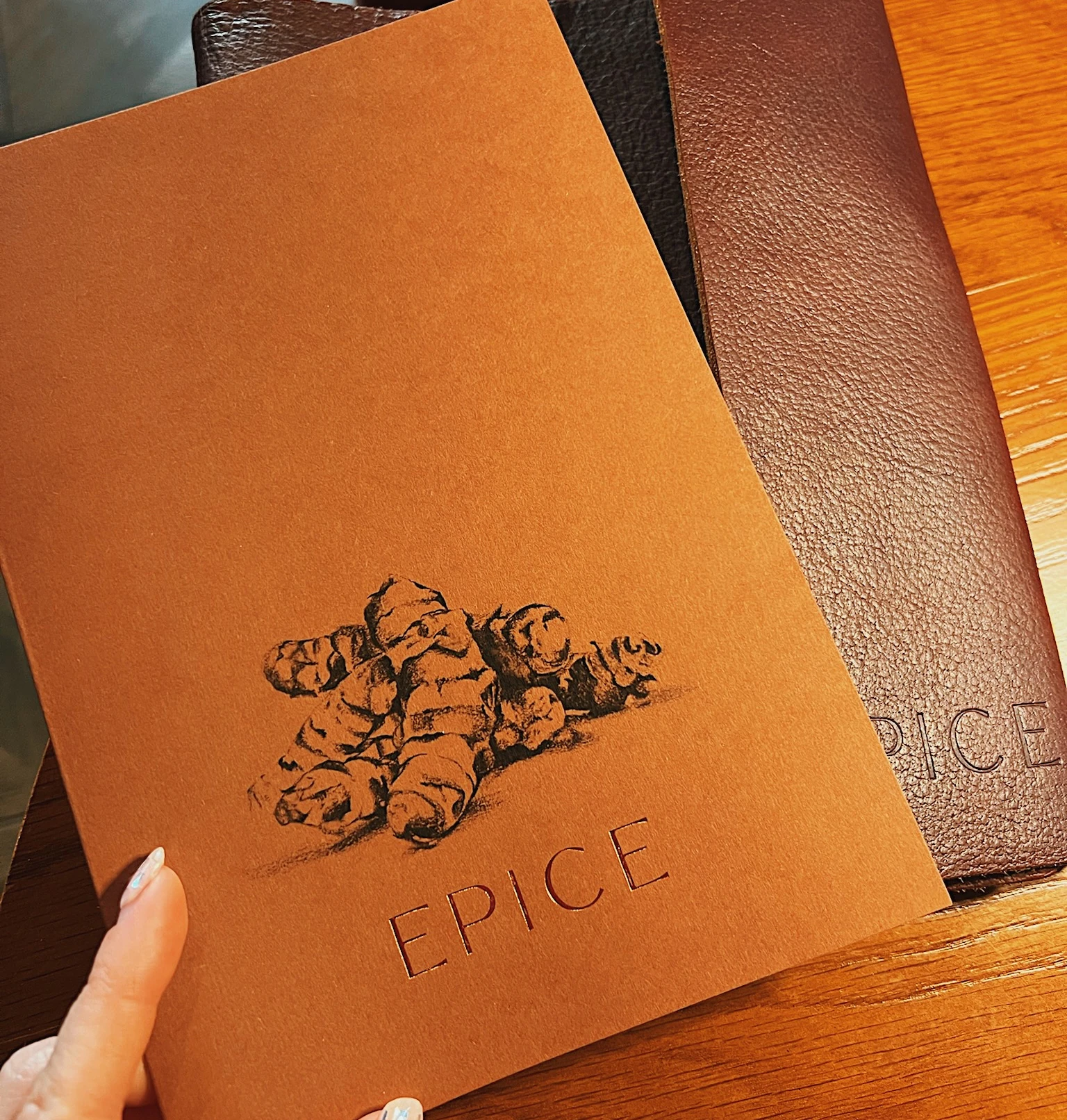 Brown EPICE menu held over a wooden restaurant table