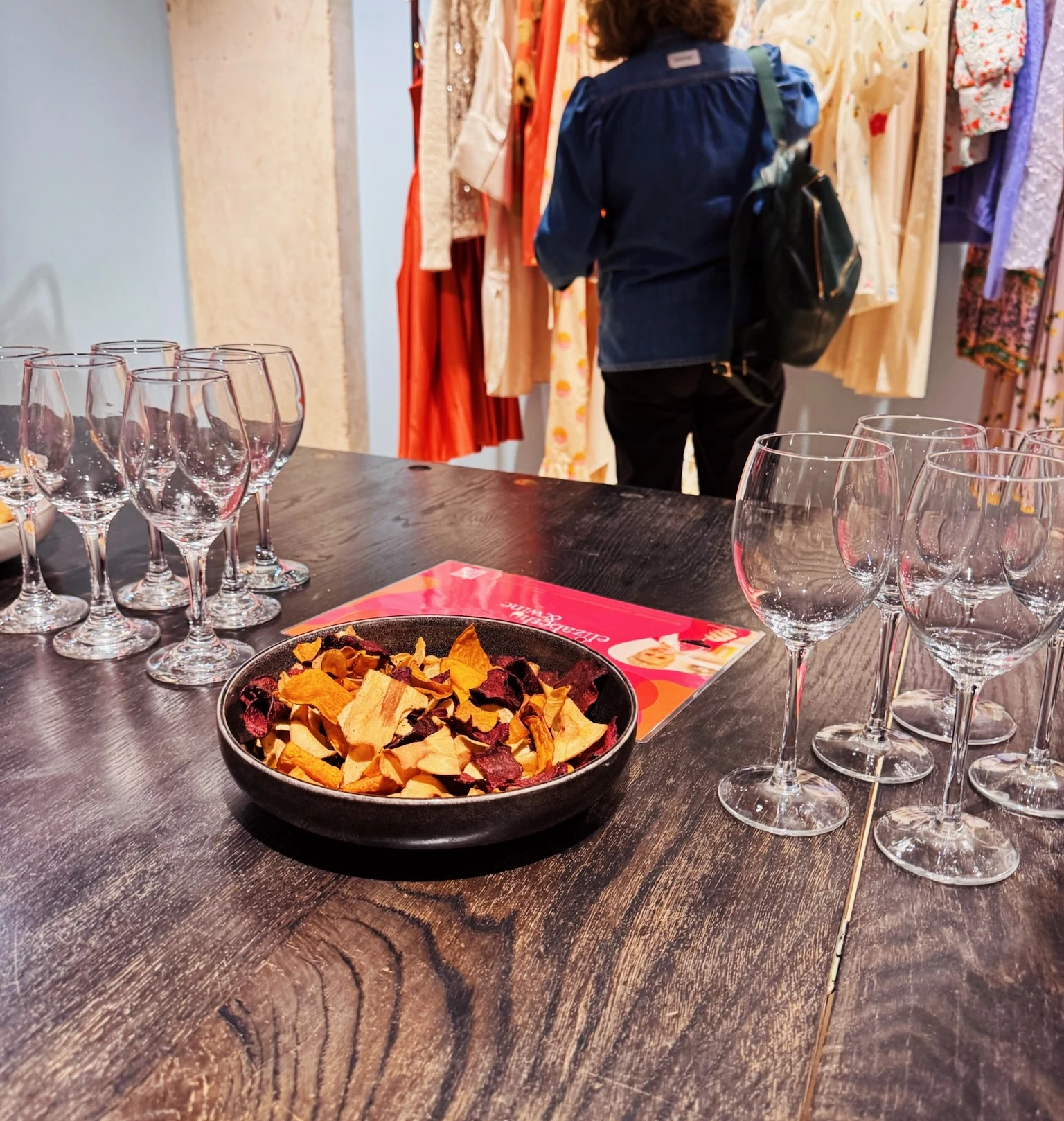 Wine glasses and vegetable crisps on a table beside a clothing rail