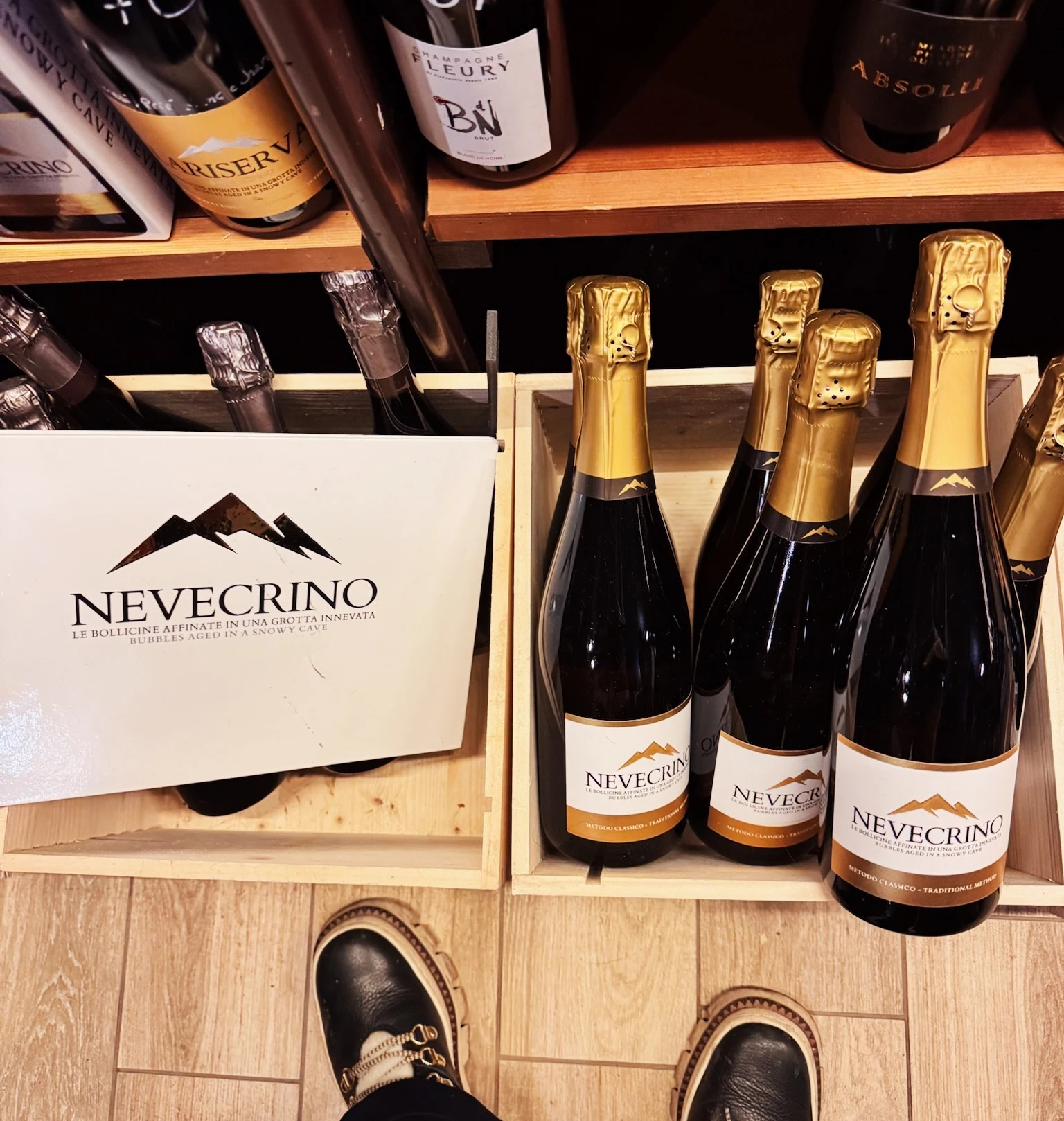 Bottles of Nevecrino sparkling wine displayed in wooden crates, with further wines on shelves above.
