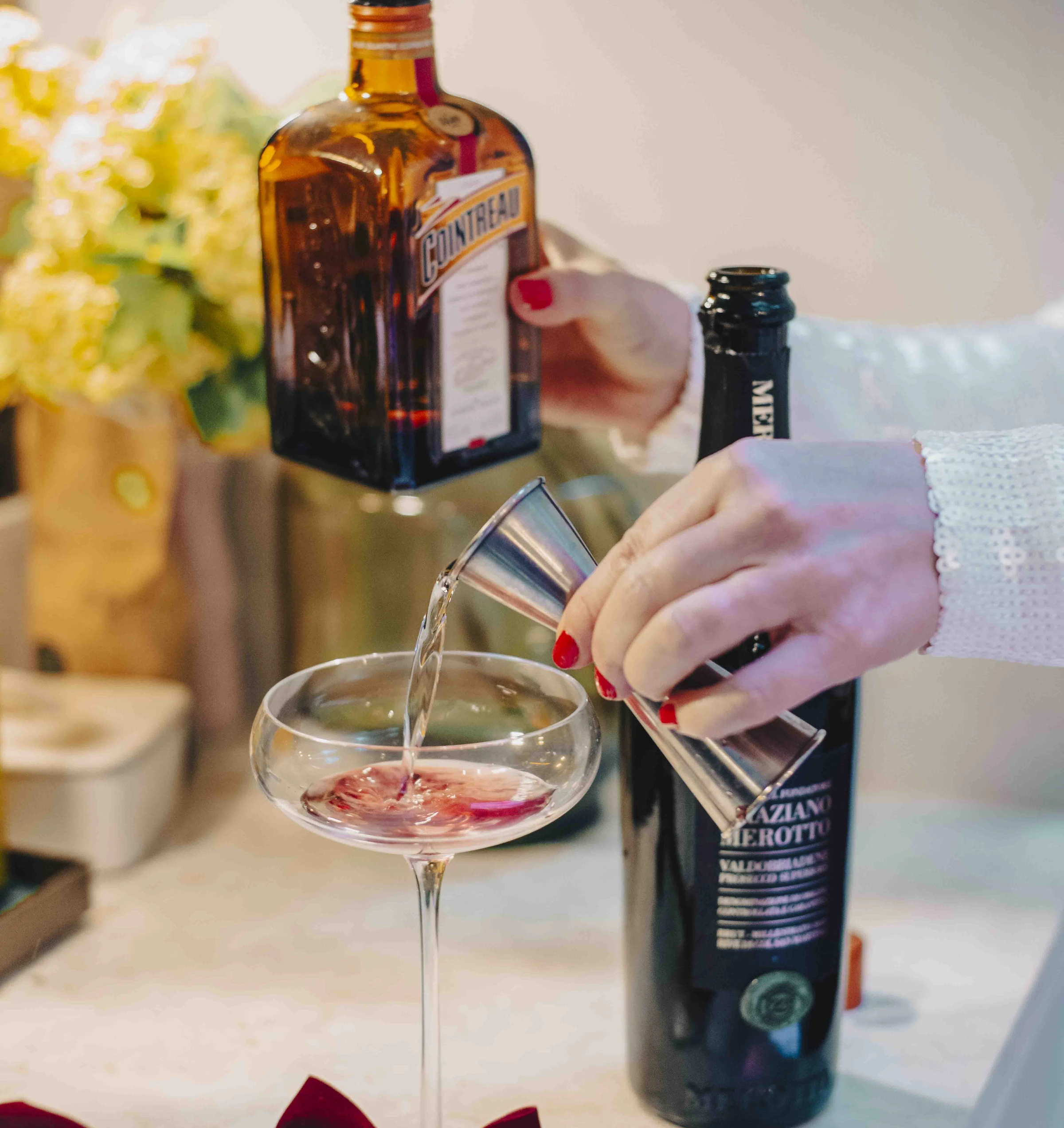 A cocktail is poured into a coupe beside Cointreau and a decorated bottle