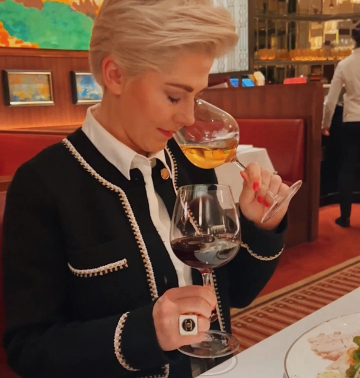 Diner smelling white wine at a restaurant table beside a glass of red wine