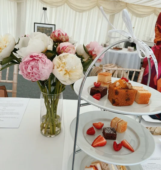 Afternoon tea stand with cakes, sandwiches and peonies beneath a draped marquee ceiling