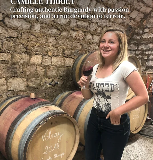 Woman holding a glass of red wine beside barrels in a stone wine cellar