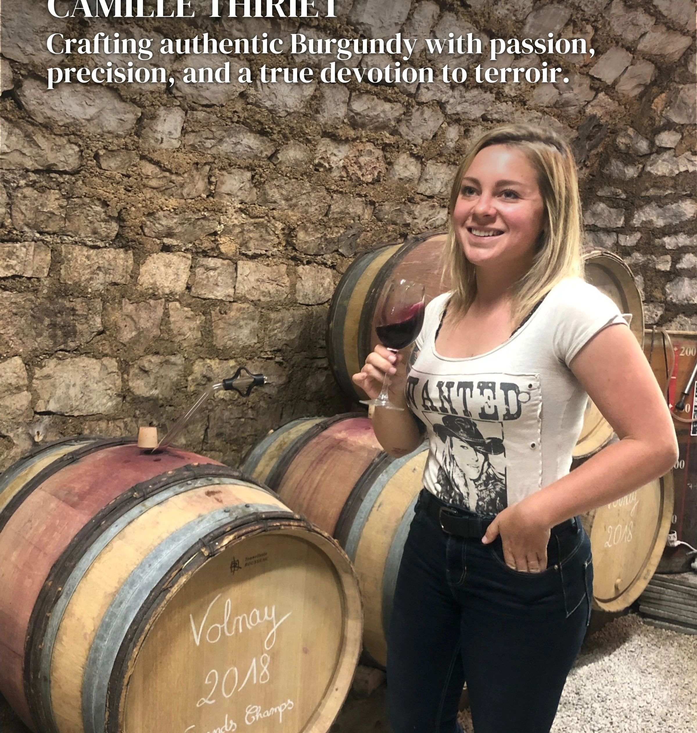 Woman holding a glass of red wine beside barrels in a stone wine cellar
