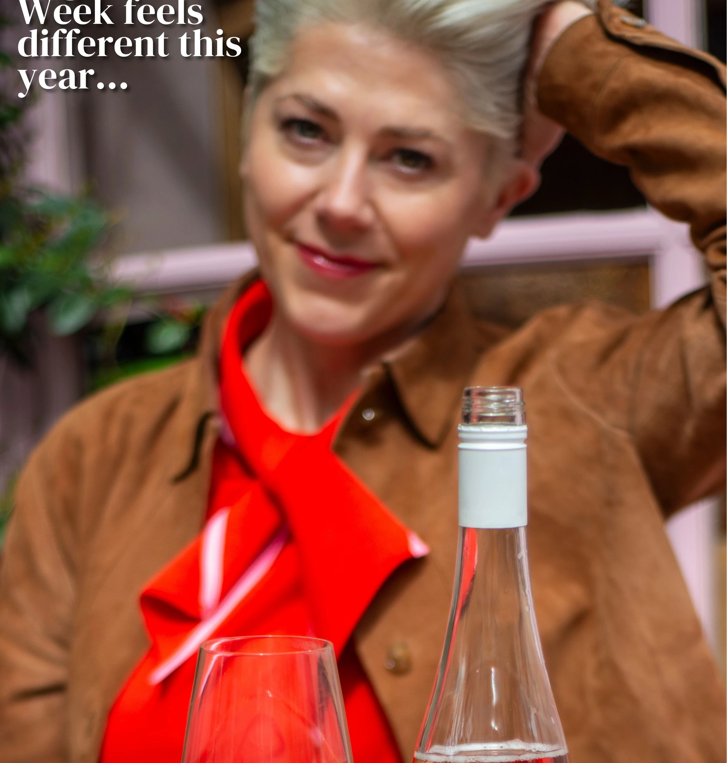 Person in a brown jacket and red top behind a glass and open bottle of wine