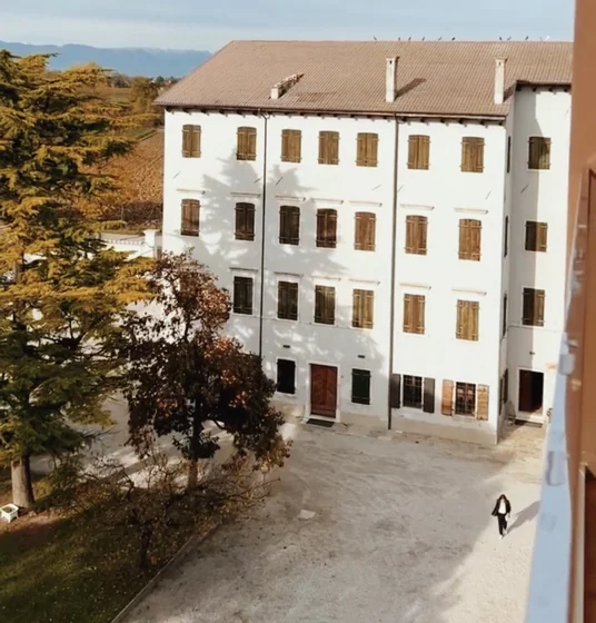 Historic white building with wooden shutters, trees and mountains in the distance