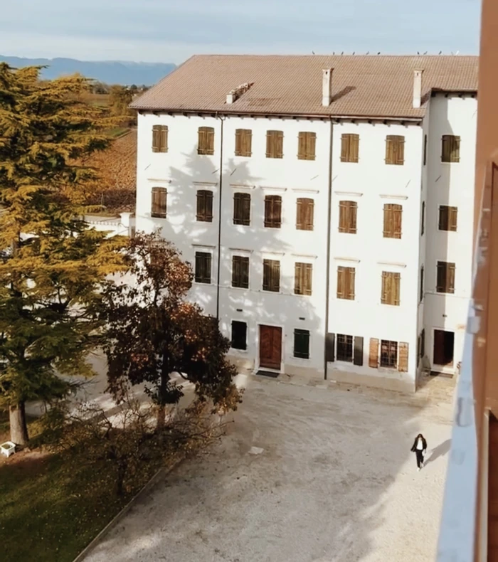 Historic white building with wooden shutters, trees and mountains in the distance