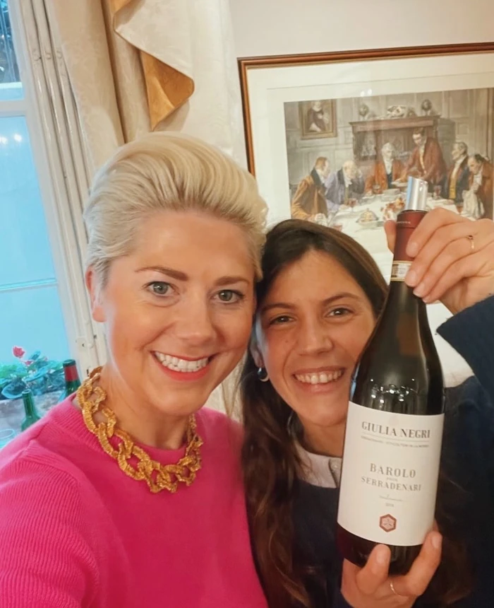 Two women smile beside a bottle of Giulia Negri Barolo Serradenari wine.
