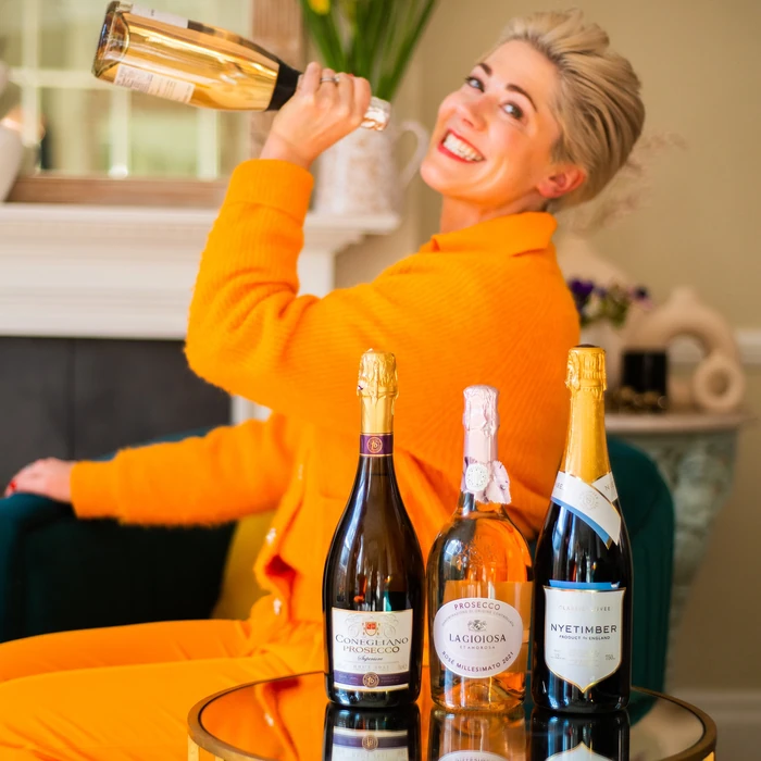 Smiling woman holding sparkling wine bottle beside three bottles