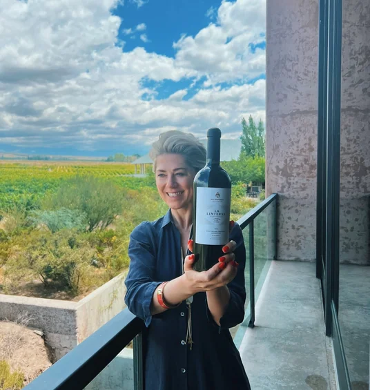 Smiling woman holding a bottle of Bemberg La Linterna wine beside a vineyard