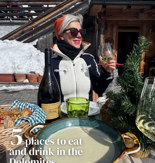 Woman holding a glass of white wine beside a bottle and alpine restaurant table in the snow
