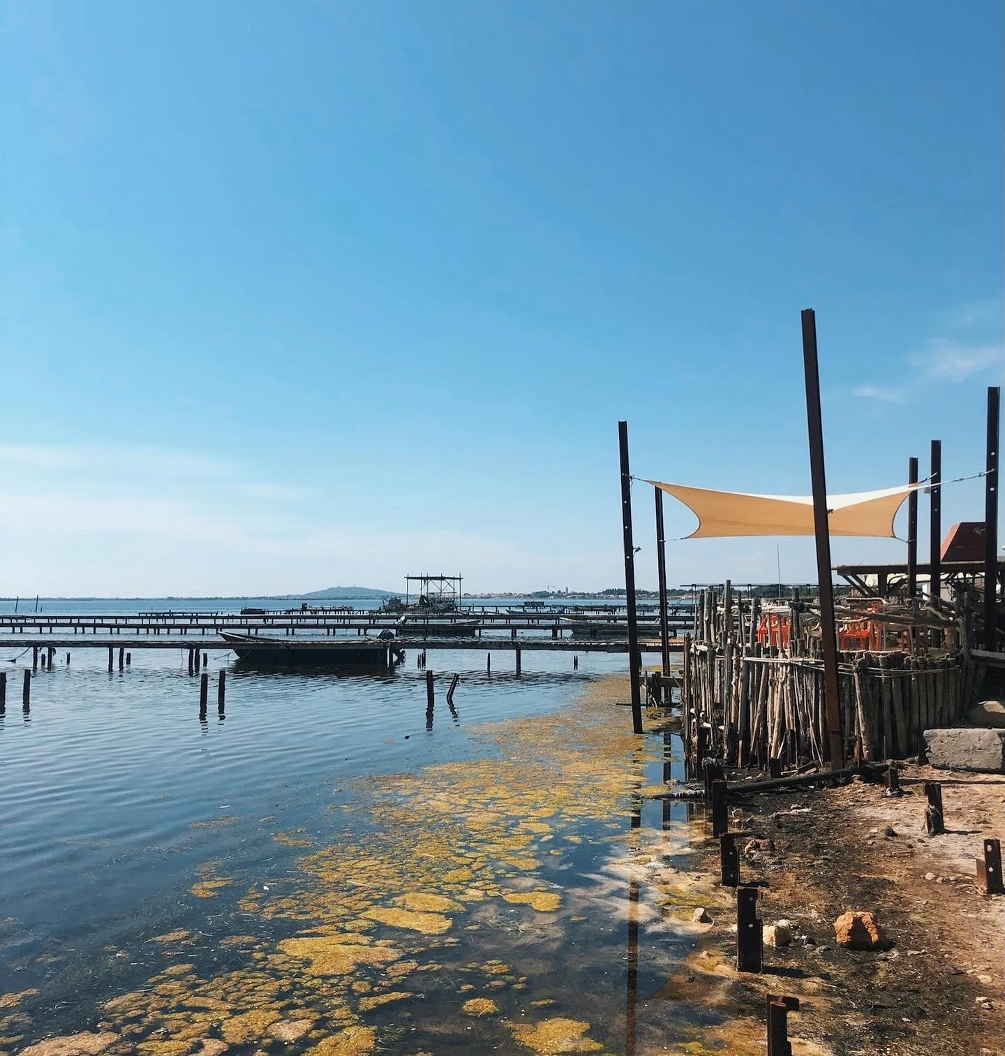 Oyster beds and waterfront structures beside a sunshade on a bright blue day