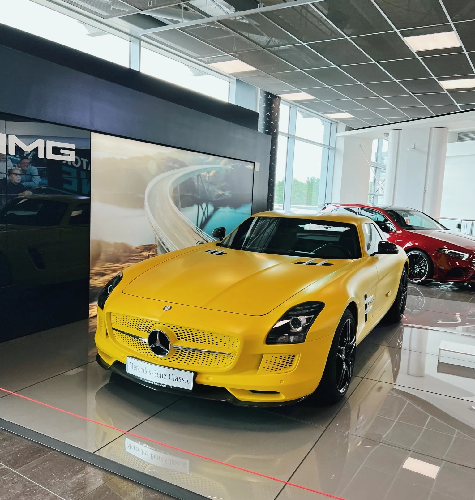 Yellow Mercedes-Benz sports car displayed beside a red car in a bright showroom