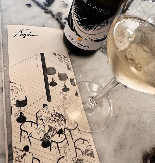 Klaus Lentsch Pinot Bianco beside a glass of white wine and an Osteria Angelina menu