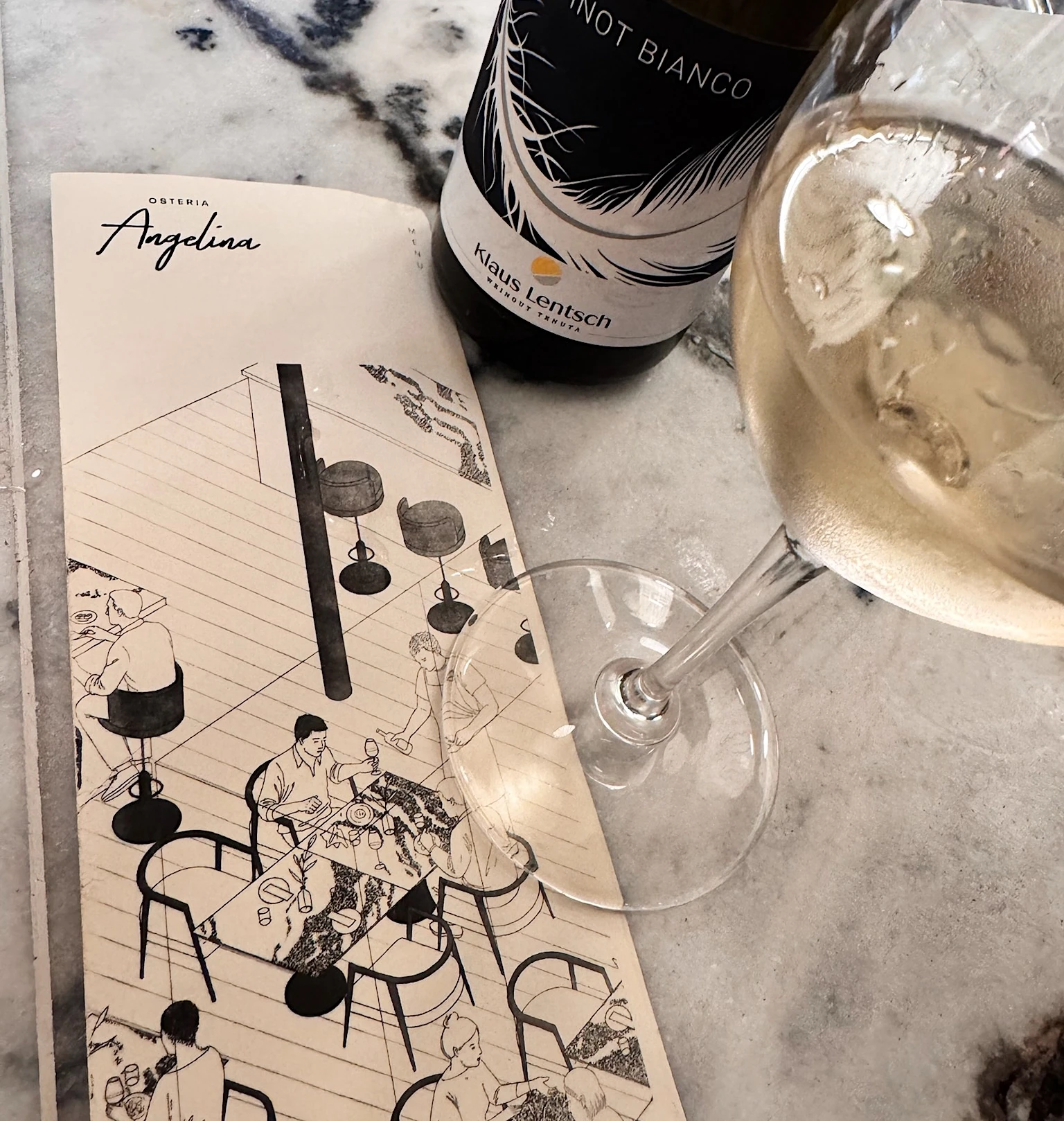 Klaus Lentsch Pinot Bianco beside a glass of white wine and an Osteria Angelina menu