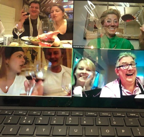 Laptop screen showing a virtual wine tasting, with four video-call panels and participants holding wine glasses.