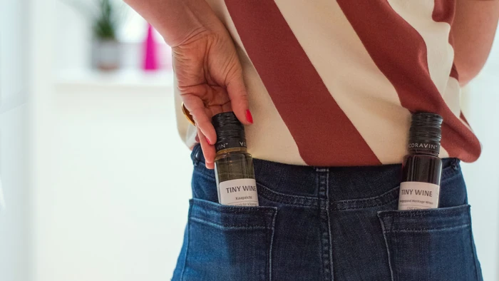 Person holding two tiny wine bottles in jeans pockets