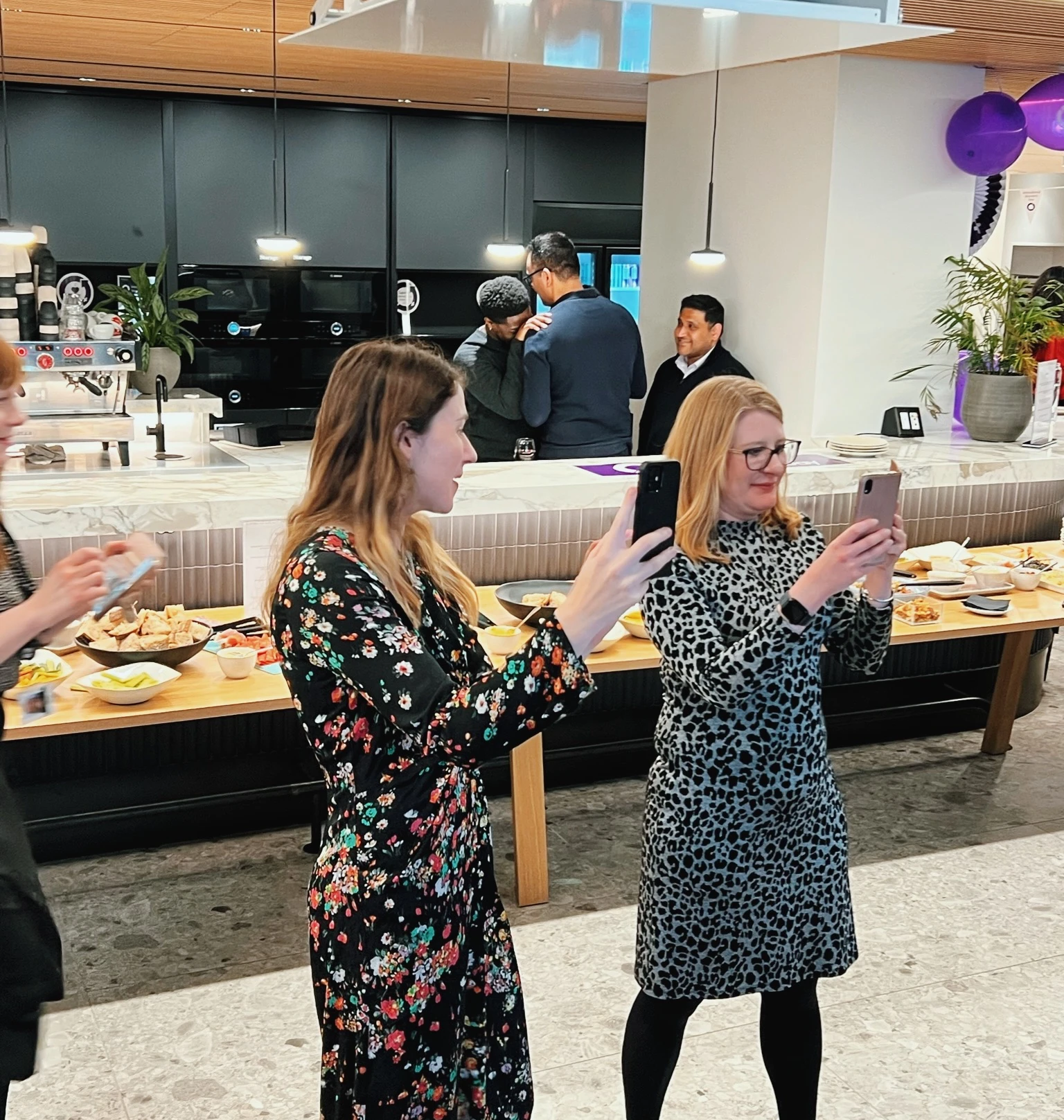 Guests use their phones at a lively corporate event with food, drinks and purple balloons