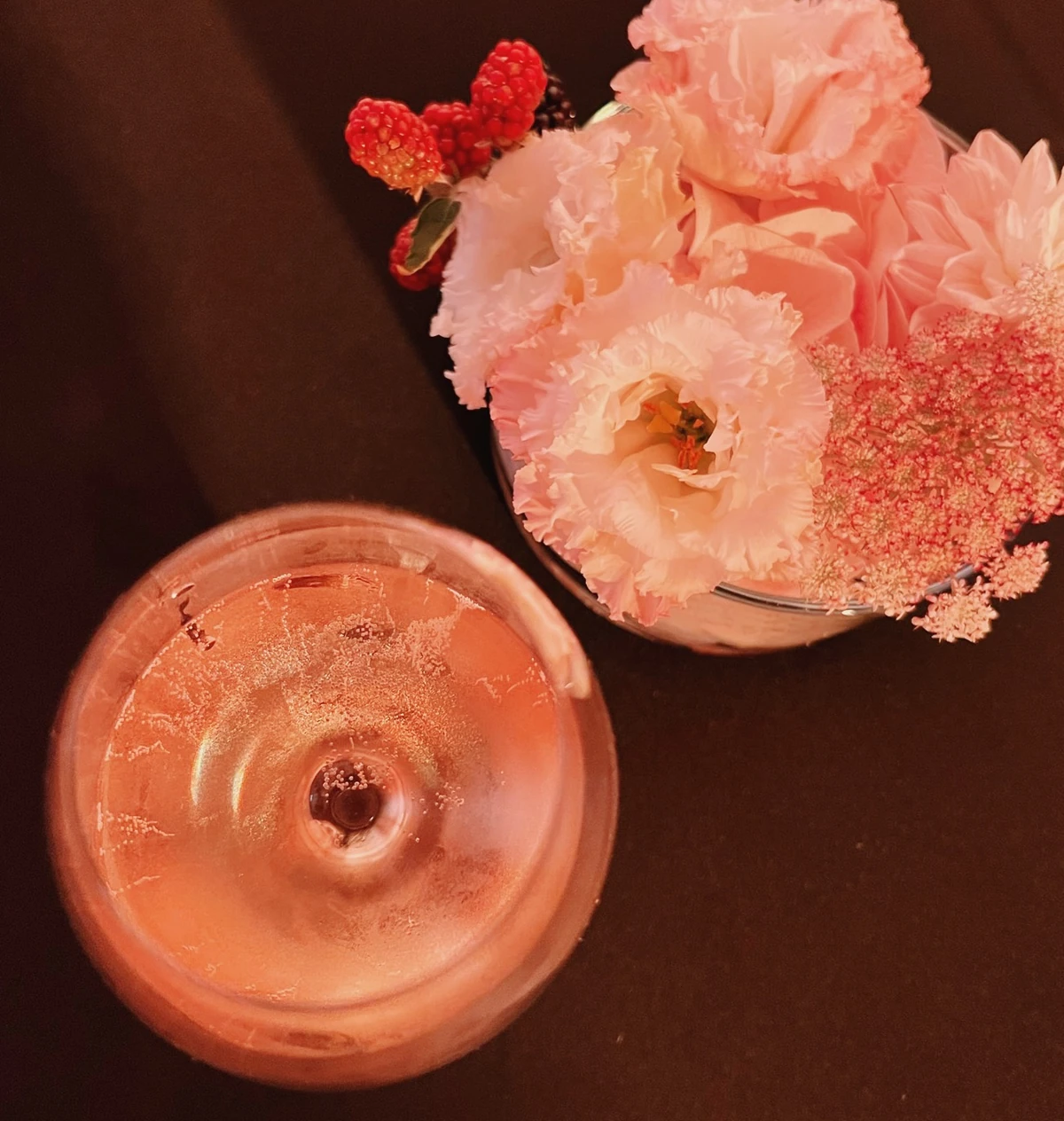 Overhead view of a glass of rosé Champagne beside a bouquet of pink flowers and raspberries