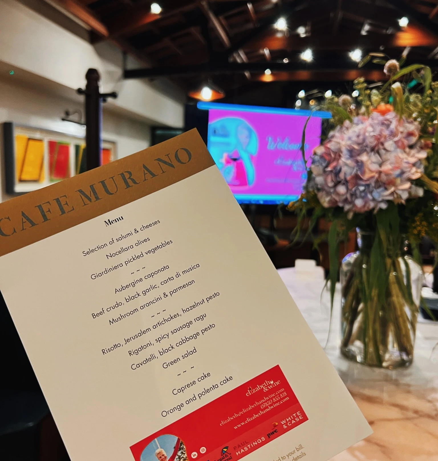 Caffè Murano menu beside a floral arrangement in a warmly lit event space