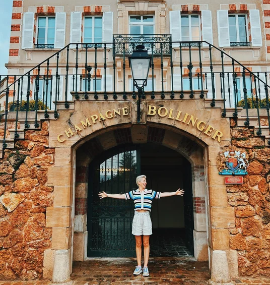 Person with arms outstretched beneath the Champagne Bollinger entrance