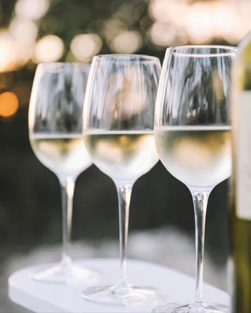 Three white wine glasses on a table outdoors
