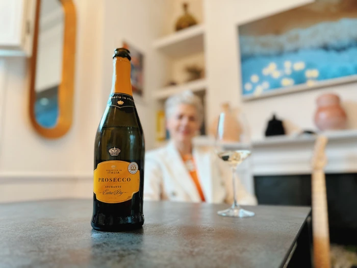 Prosecco bottle on table with blurred wine host in background