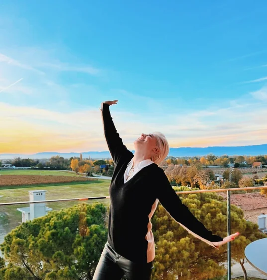 Elizabeth poses on a balcony overlooking vineyards and countryside beneath a blue and golden sky