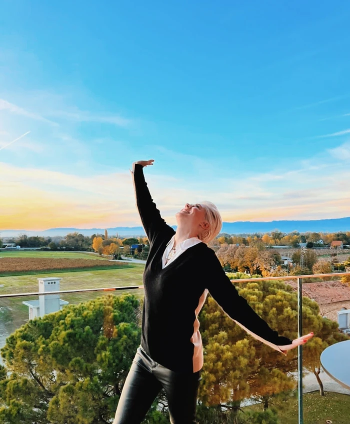 Elizabeth poses on a balcony overlooking vineyards and countryside beneath a blue and golden sky