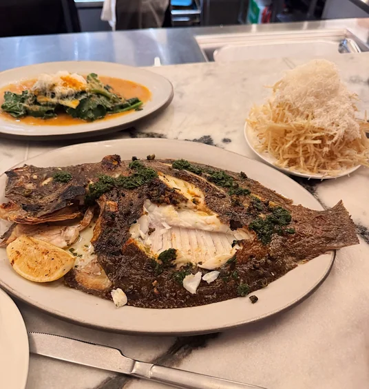 Whole grilled fish with greens, sauce and crispy potato garnish on a restaurant counter