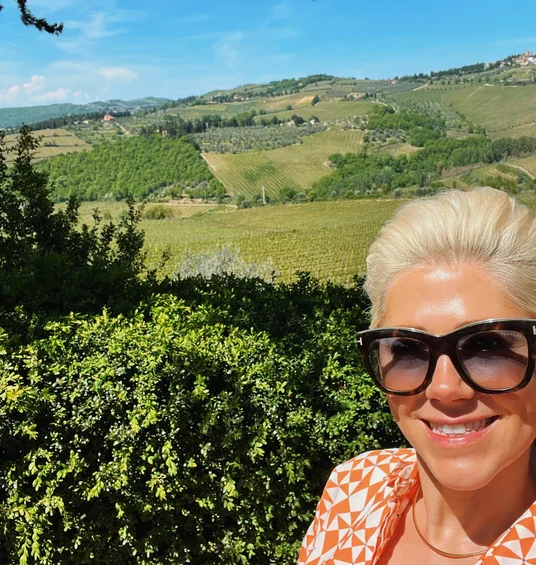 Elizabeth smiles in sunglasses before rolling Tuscan vineyards and hills at Fontodi Winery.