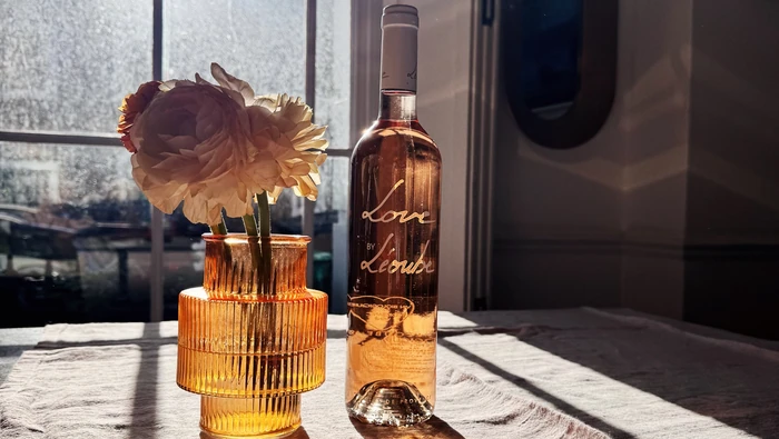 Rosé wine bottle beside flower in amber glass vase by window