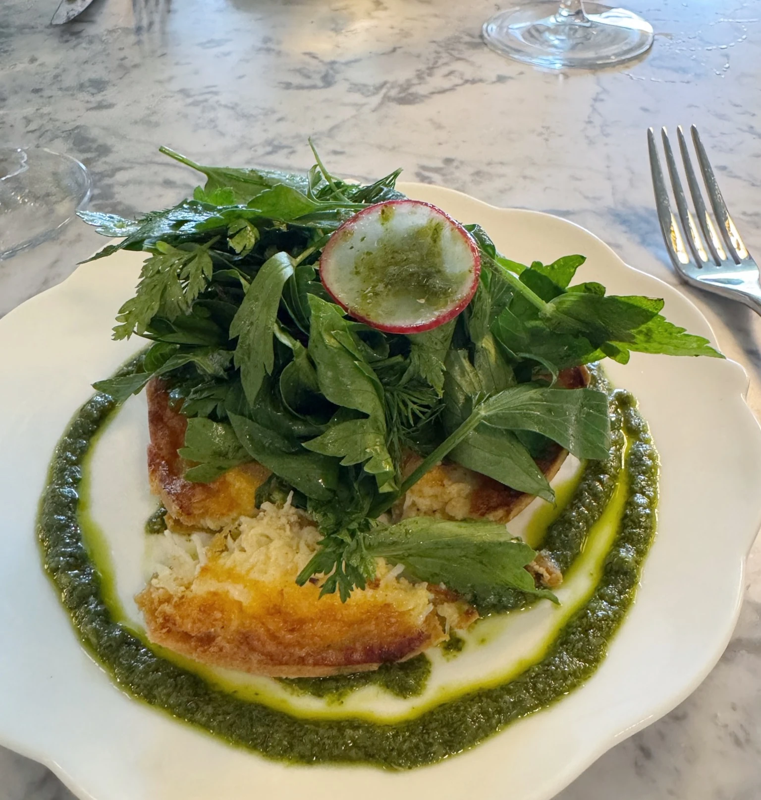 Breaded dish topped with fresh herbs and radish, served with green sauce