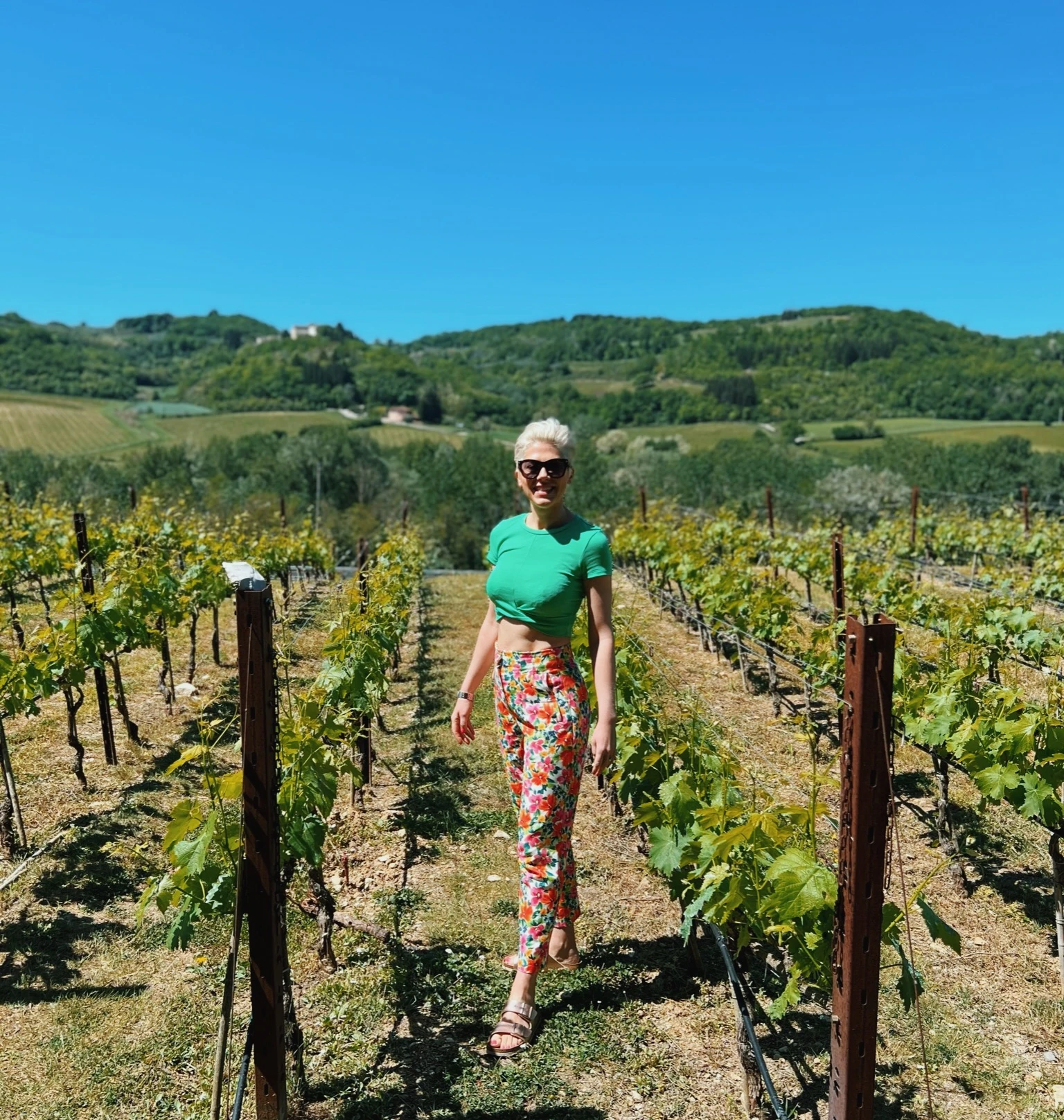 Woman walking between rows of vines at Antinori winery in Tuscany, with rolling hills behind