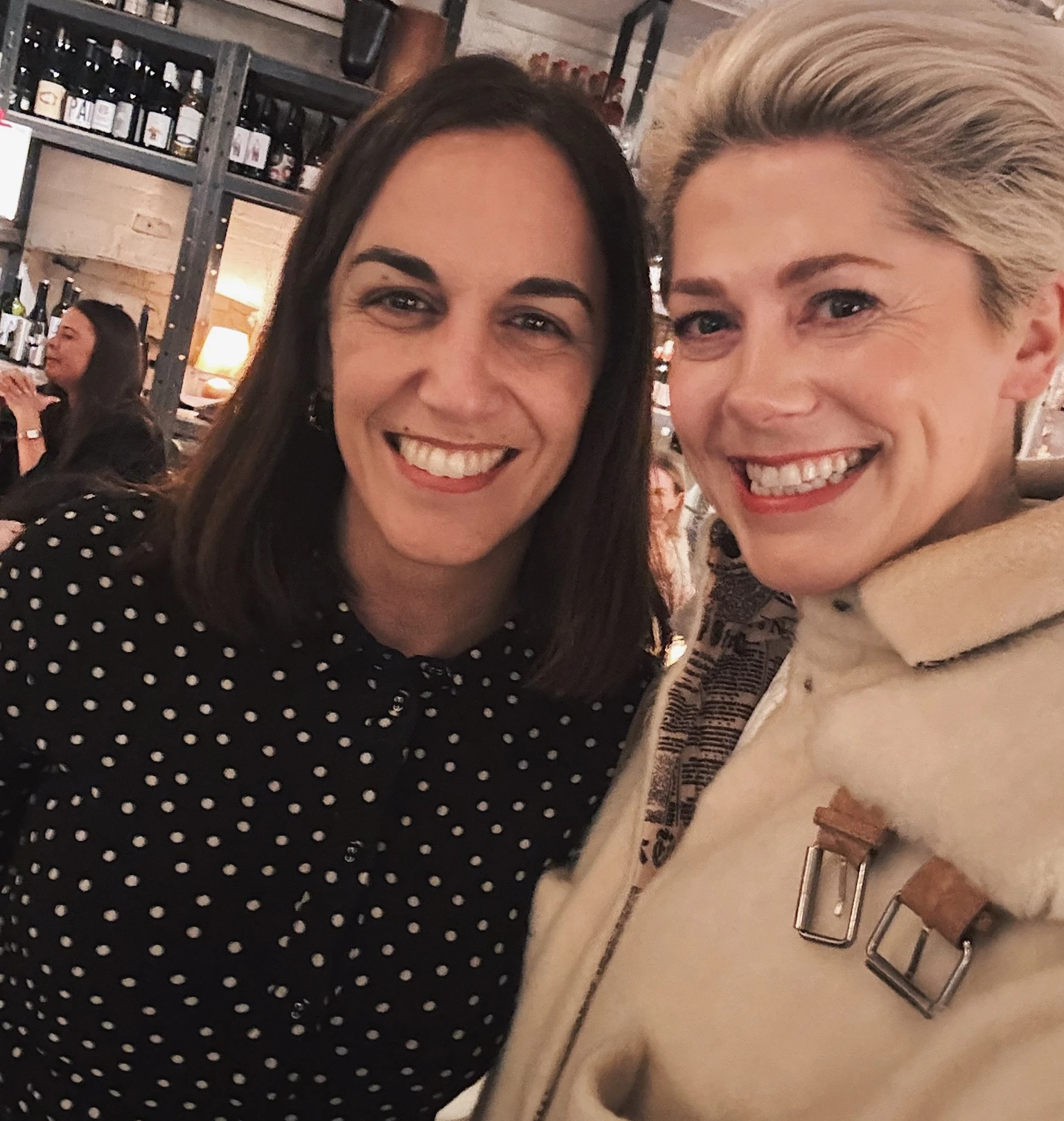 Two smiling women pose together inside a bottle-filled farm shop