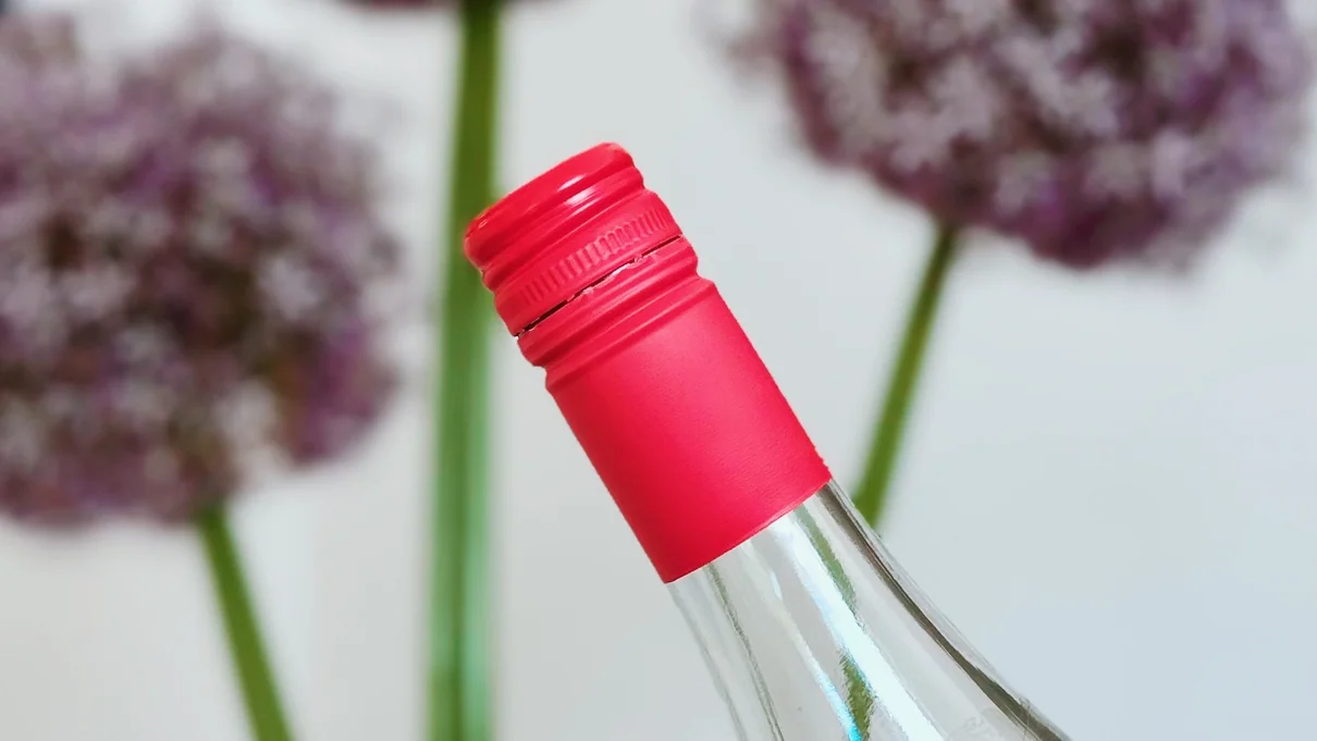 Close-up of wine bottle neck with red cap and blurred flowers